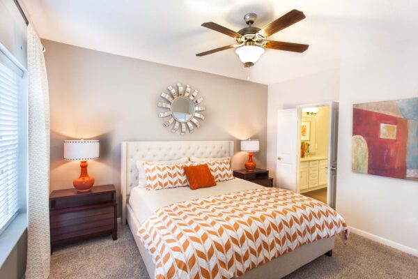 Prairie View at Village West apartment bedroom with plush carpet, bed with headboard, ceiling fan, and decorative mirror.