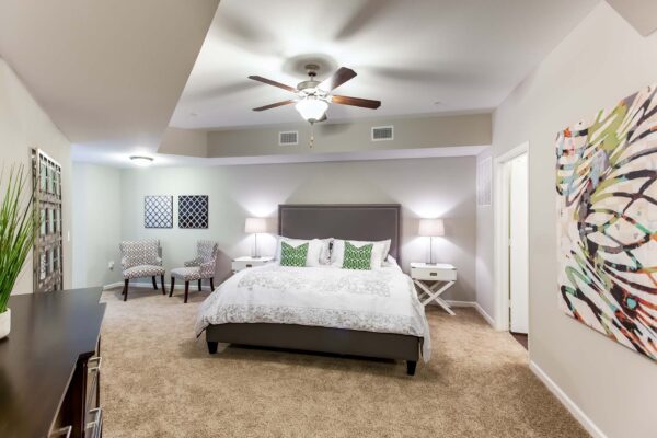 Prairie View at Village West apartment bedroom with plush carpet, bed with headboard, armchairs, and ceiling fan.