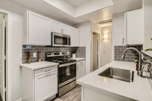 Springs at Alta Mesa apartment kitchen with wood style floor, white cabinets, light counters, and stainless steel appliances.