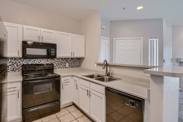 Springs at Alta Mesa apartment kitchen with tile floor, white cabinets, tiled backsplash, and black appliances.