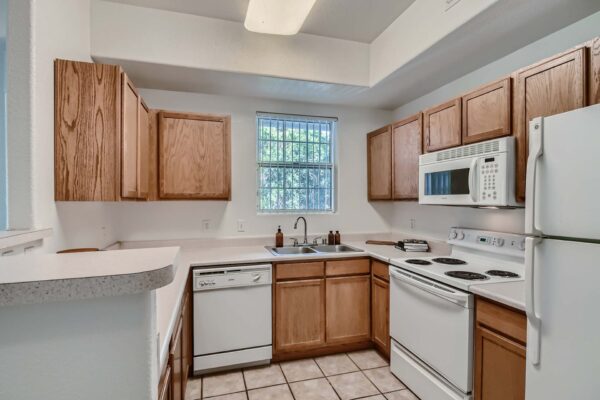Springs at Alta Mesa apartment kitchen with tile floor, wood cabinets, gray counters, and white appliances.
