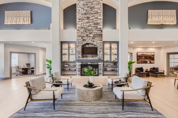 Springs at Alta Mesa apartment lobby with modern armchairs, stone fireplace, TV, and shelves with decor.