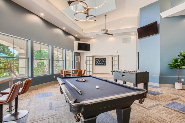 Springs at Alta Mesa apartments clubhouse with pool table, foosball, wall mounted TVs, and large windows.