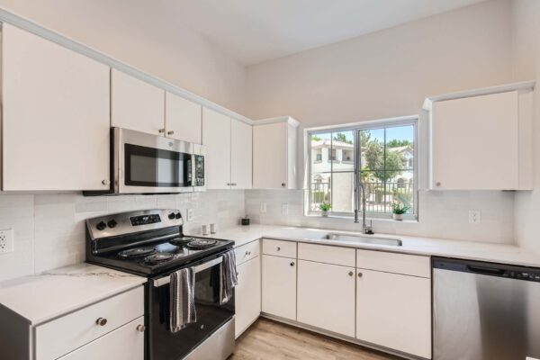 Springs at Alta Mesa apartment kitchen with wood style floor, white cabinets and counters, and stainless steel appliances.