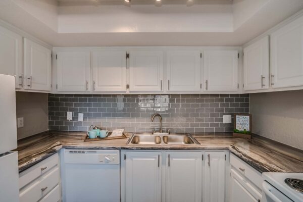Tempe Vista apartment kitchen with white cabinets, dark counters, tiled backsplash, and white appliances.