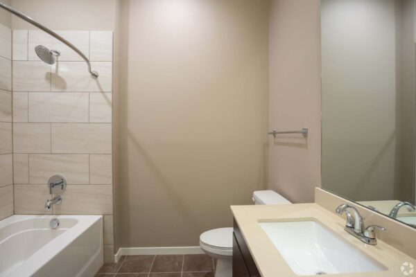 The Locale apartment bathroom with tile floor, dark cabinets, light counters, and tiled shower tub.