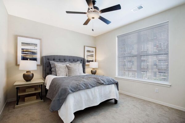 The Locale apartment bedroom with carpet, plush bed with headboard, bedside tables with lamps, and ceiling fan.