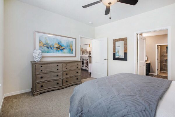 The Locale apartment bedroom with carpet, plush bed, dresser with decor, and large artwork.