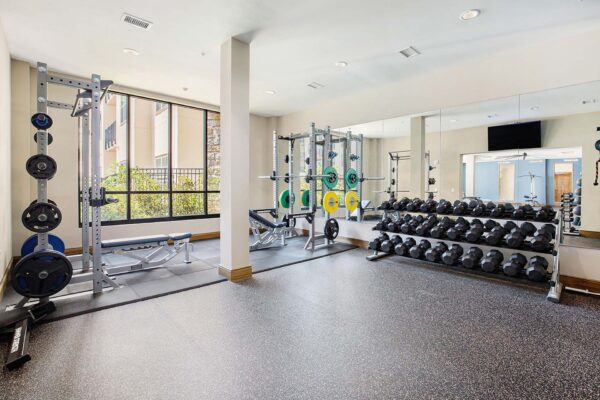 The Locale apartments fitness center with weight equipment, mirror wall, and large windows.