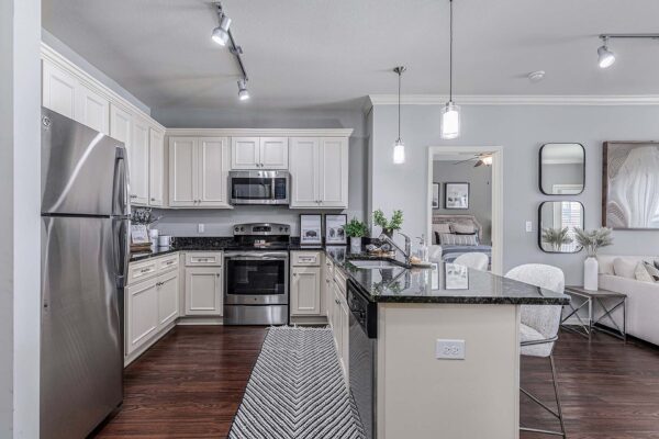 Village West apartment kitchen with wood style floor, light cabinets, dark counters, and stainless steel appliances.