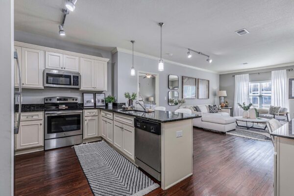 Village West apartment kitchen with wood style floor, light cabinets, dark counters, and stainless steel appliances.
