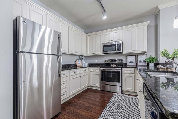 Village West apartment kitchen with wood style floor, light cabinets, dark counters, and stainless steel appliances.