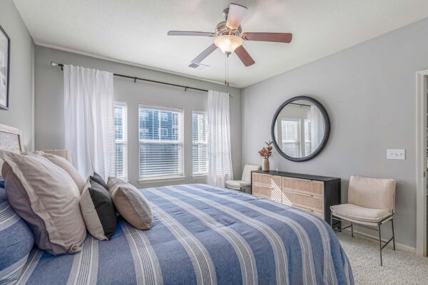 Village West apartment bedroom with carpet, plush bed, dresser, and large round mirror.