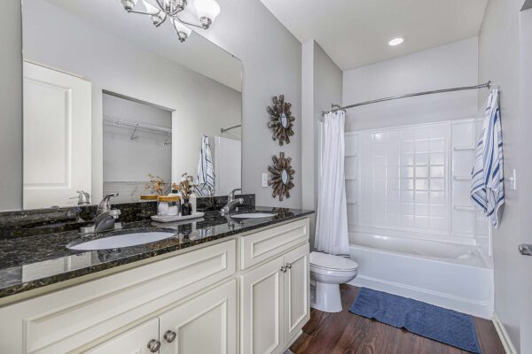 Village West apartment bathroom with wood style floor, light cabinets, dark counters, and large mirror.