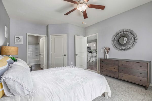 Village West apartment bedroom with carpet, plush bed, dresser, and decorative mirror.