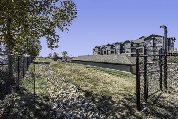 Village West apartments dog run with grassy hill and trees.