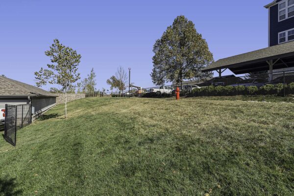 Village West apartments dog run with grassy hill and trees.