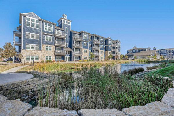 Village West apartments pond with lush grasses and fountain.