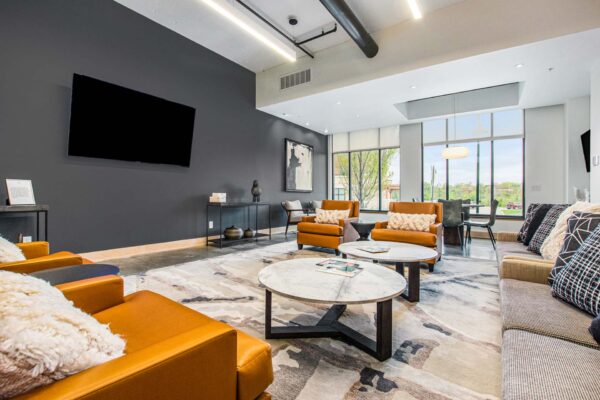 Village at Mission Farms apartments lounge with plush seating, wall mounted TV, and large windows.