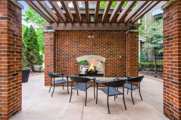 Village at Mission Farms apartments outdoor lounge with brick fireplace, pergola, and chairs.