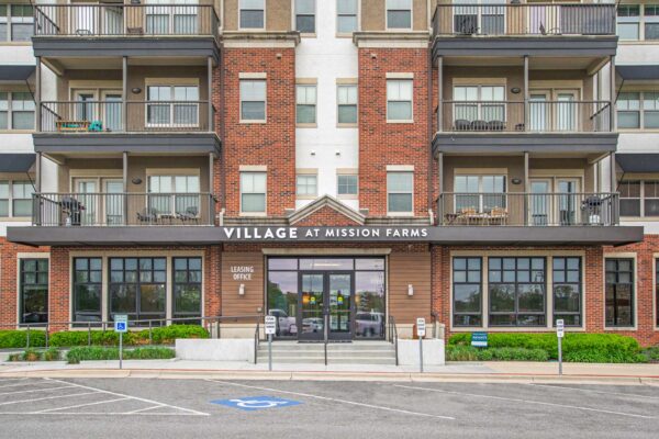 Village at Mission Farms apartments entrance with classic brick construction and ample parking.
