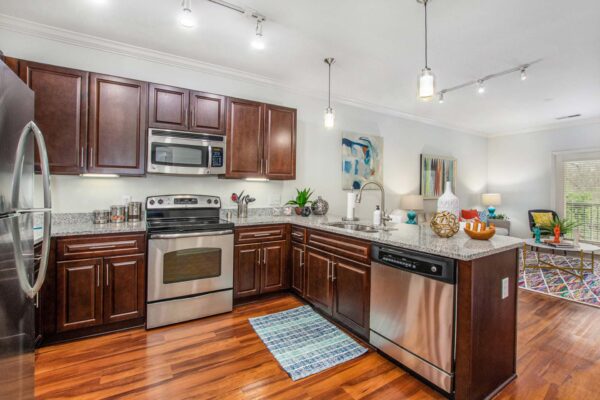 Village at Mission Farms apartment kitchen with wood style floor and cabinets, stone counters, and stainless steel appliances.