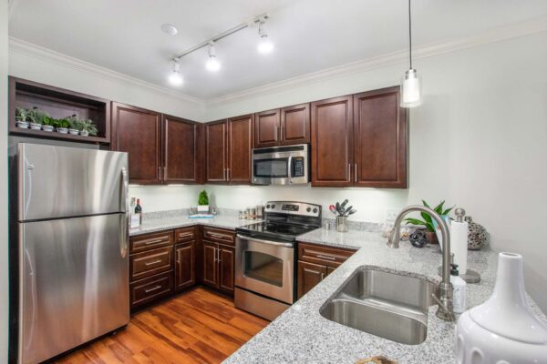 Village at Mission Farms apartment kitchen with wood style floor and cabinets, stone counters, and stainless steel appliances.