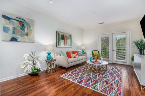 Village at Mission Farms apartment living room with wood style floor, pattern rug, plush couch, and balcony door.