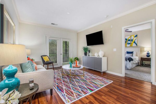 Village at Mission Farms apartment living room with wood style floor, colorful rug, plush couch, and balcony door.