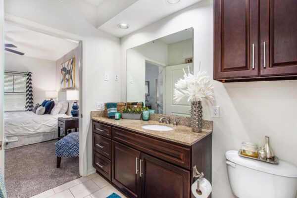 Village at Mission Farms apartment bathroom with tile floor, wood cabinets, stone counters, and large mirror.