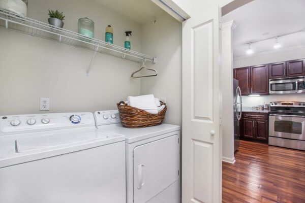 Village at Mission Farms apartment laundry room with washer, dryer, and built in shelves with cleaning supplies.