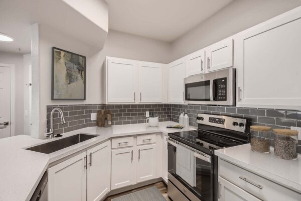 Villas at Mountain Vista Ranch apartment kitchen with white cabinets and counters, tiled backsplash, and stainless steel appliances.