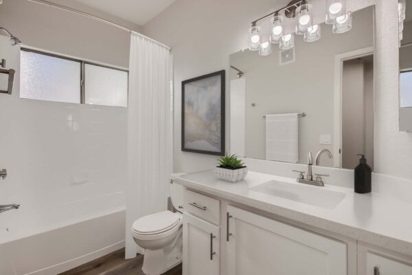 Villas at Mountain Vista Ranch apartment bathroom with white cabinets and counters, large mirror, and tiled shower tub.