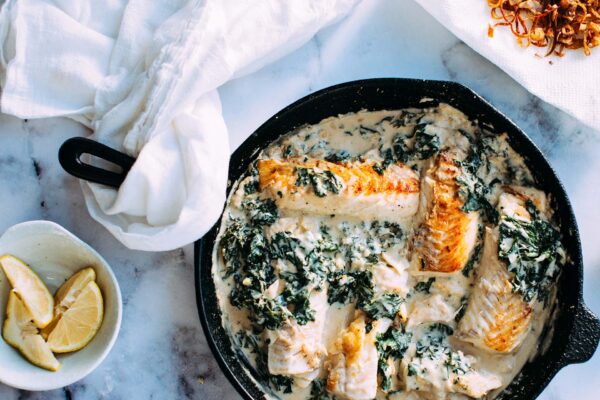 Skillet with fish filets in a cream sauce with spinach.
