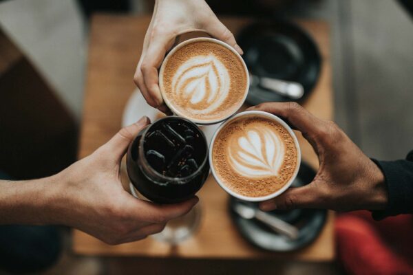 Three friends toasting together at cafe with coffee drinks.