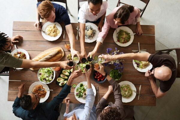 Friends toasting with cocktails at dinner table with elegant meals.