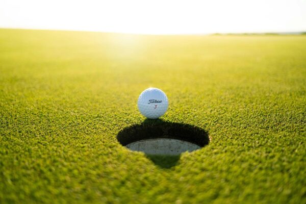 Golf ball on edge of hole on smooth putting green.