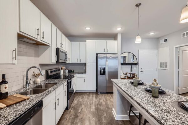 The Avery apartment kitchen with wood style floor, white cabinets, stone counters, and stainless steel appliances.