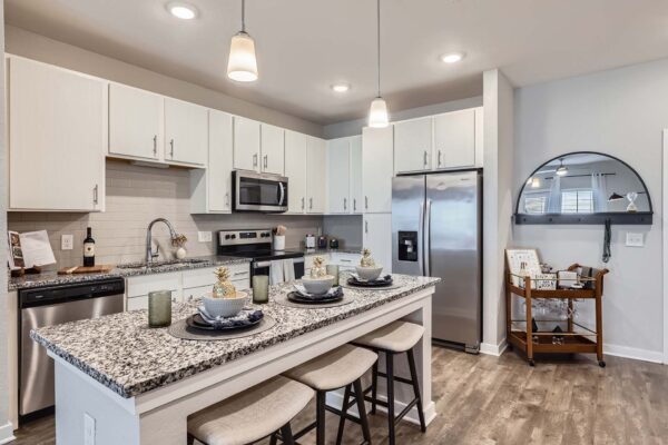 The Avery apartment kitchen with wood style floor, white cabinets, stone counters, and stainless steel appliances.