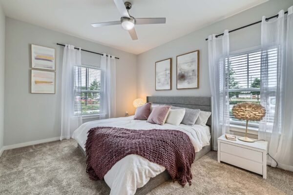The Avery apartment bedroom with carpet, plush bed with headboard, and large windows.