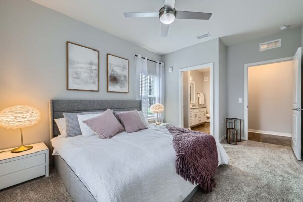 The Avery apartment bedroom with carpet, plush bed with headboard, ceiling fan, and large windows.