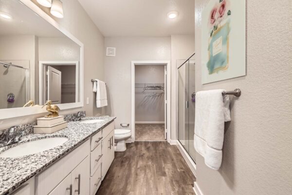 The Avery apartment bathroom with wood style floor, white cabinets, and stone counters.