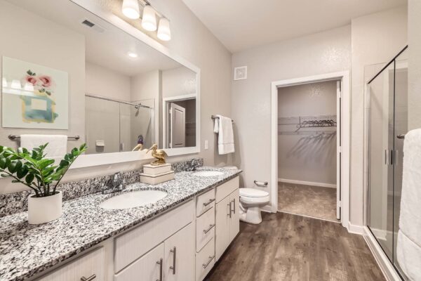 The Avery apartment bathroom with wood style floor, white cabinets, stone counters, and framed mirror.