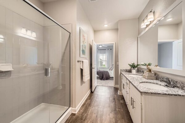 The Avery apartment bathroom with wood style floor, white cabinets, stone counters, and glass wall shower.