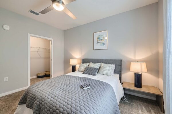 The Avery apartment bedroom with carpet, plush bed with headboard, and bedside tables with lamps.