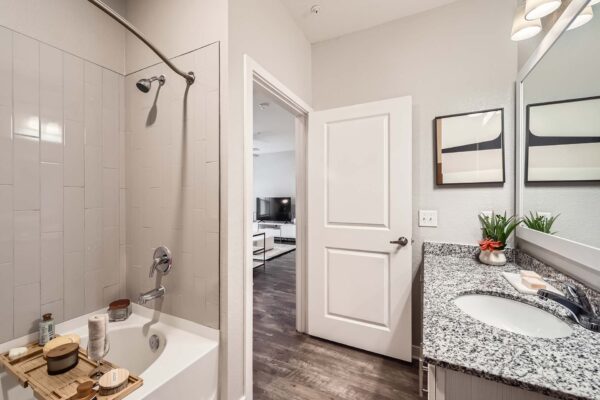 The Avery apartment bathroom with wood style floor, stone counters, framed mirror, and tiled shower tub.