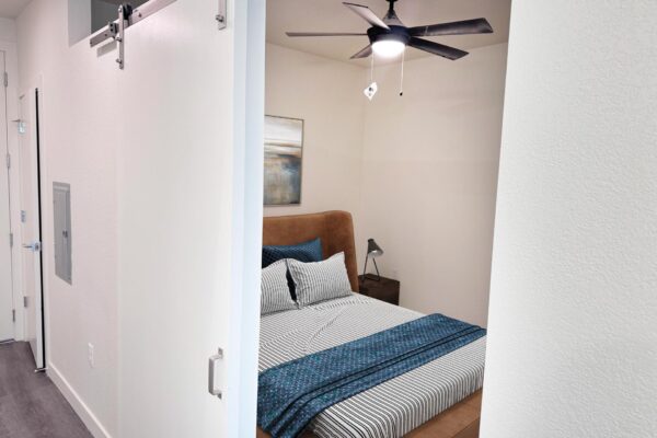 29x apartment bedroom with plush bed, framed artwork, and ceiling fan.