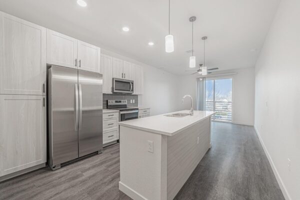 29x apartment kitchen with wood style floor, gray cabinets, light counters, pendant lights, and stainless steel appliances.