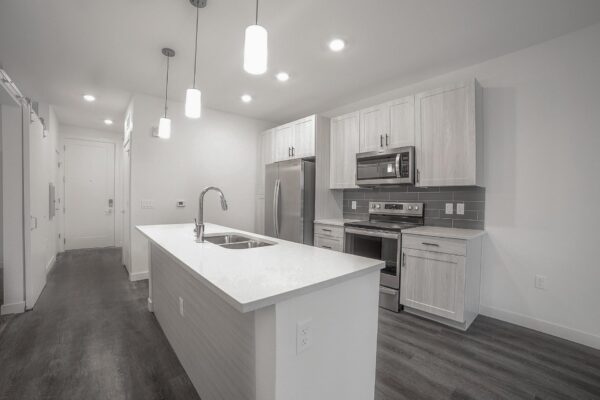 29x apartment kitchen with wood style floor, gray cabinets, light counters, stainless steel appliances, and pendant lights.