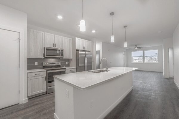 29x apartment kitchen with wood style floor, gray cabinets, light counters, pendant lights, and stainless steel appliances.